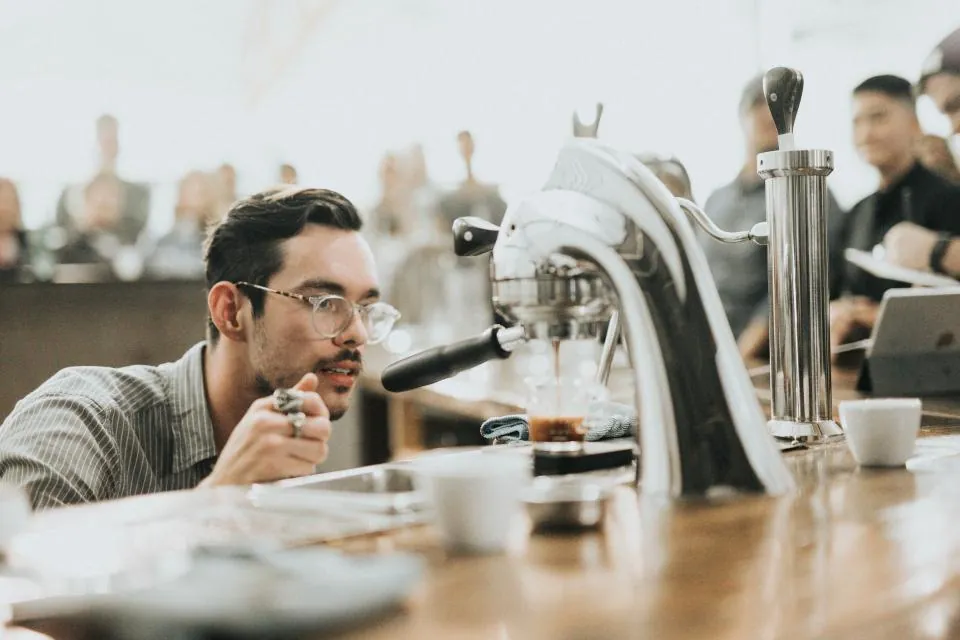 A barista tasting coffee beside an espresso machine