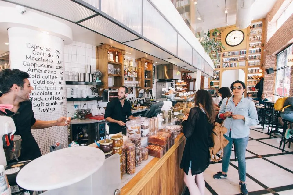 Customers ordering at a busy café counter under a menu board